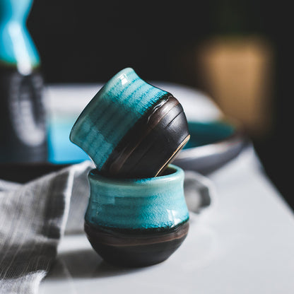 Pouring Japanese sake from a pot into two cups on a blue plate, showcasing Japanese sake pot elegance.
