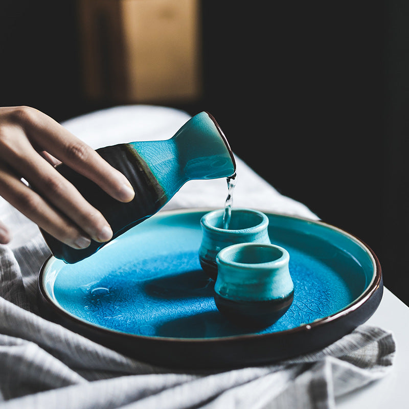 Pouring Japanese sake from a pot into two cups on a blue plate, showcasing Japanese sake pot elegance.