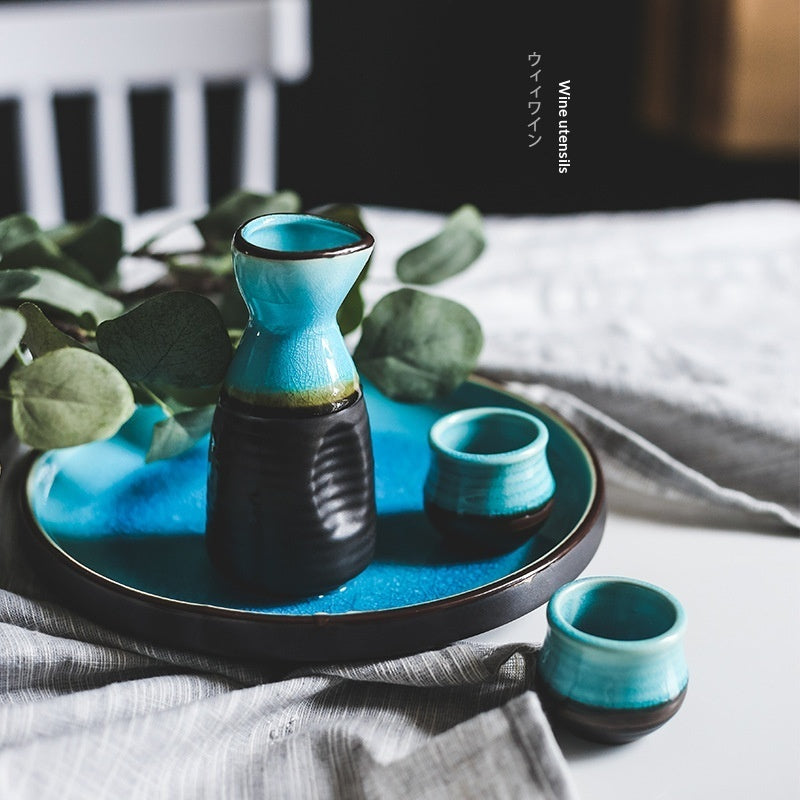 Pouring Japanese sake from a pot into two cups on a blue plate, showcasing Japanese sake pot elegance.